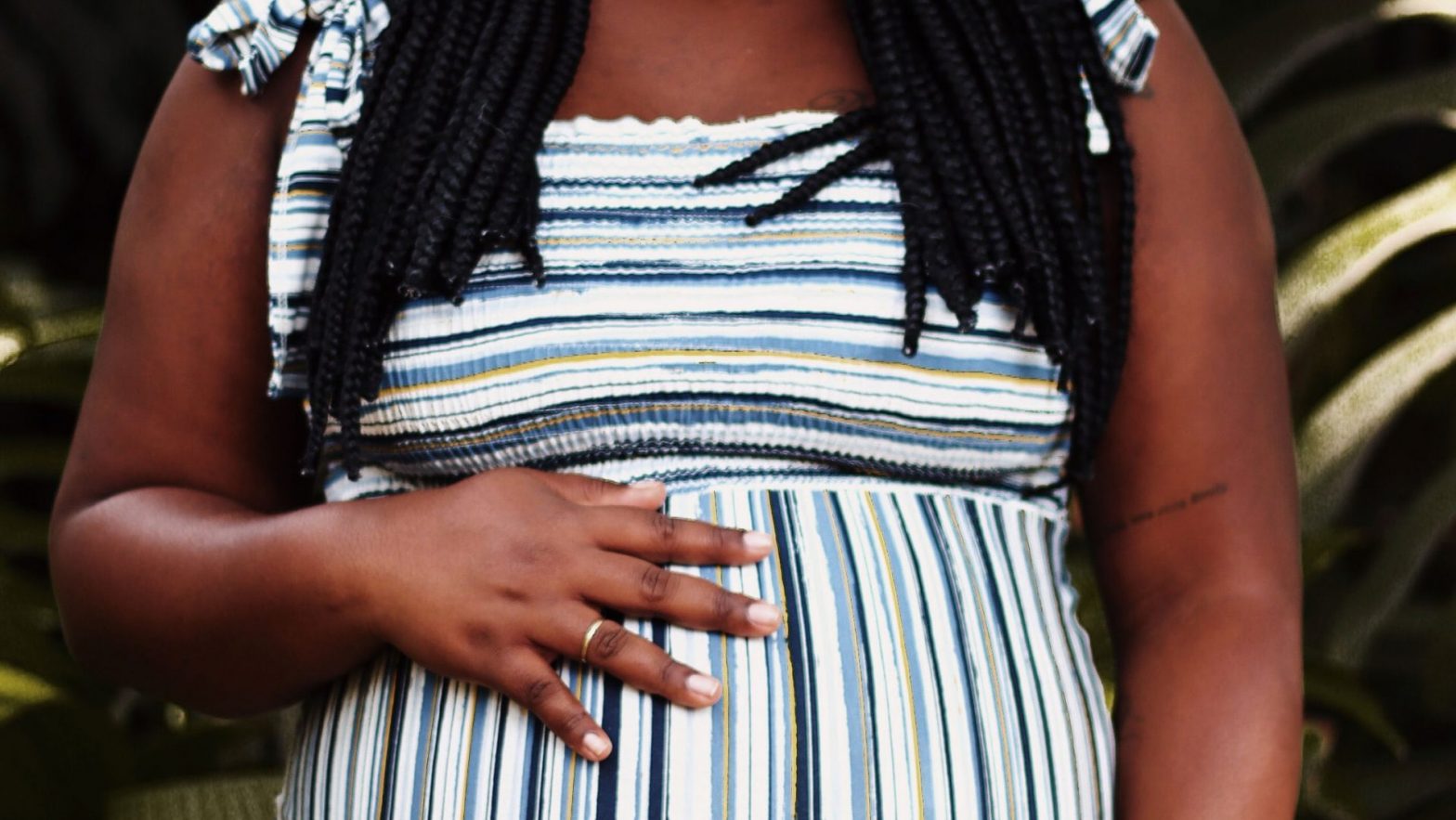 An image of a Black pregnant woman in a blue horizontal striped dress with her hand on her belly